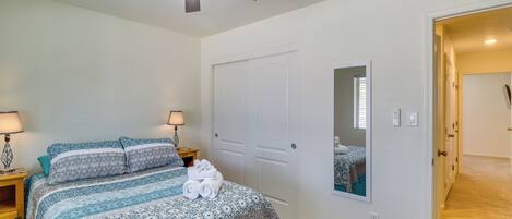 A bedroom with a bed, two bedside lamps, a ceiling fan, a door, and a wall-mounted mirror.