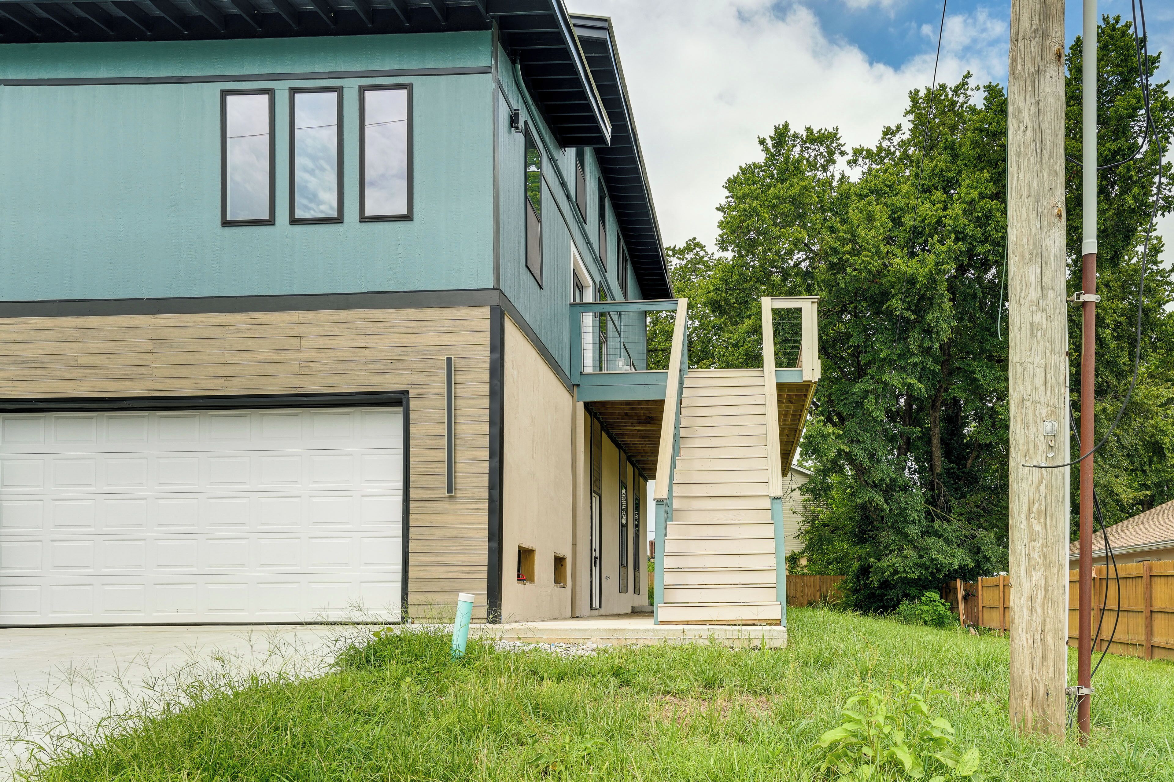 A two-story house with a garage, a balcony, and a wooden fence in the background.