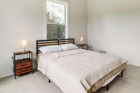 A bedroom with a bed, two bedside tables, a window, and a radiator.