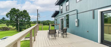 A deck with outdoor seating, a railing, and a view of a green landscape.