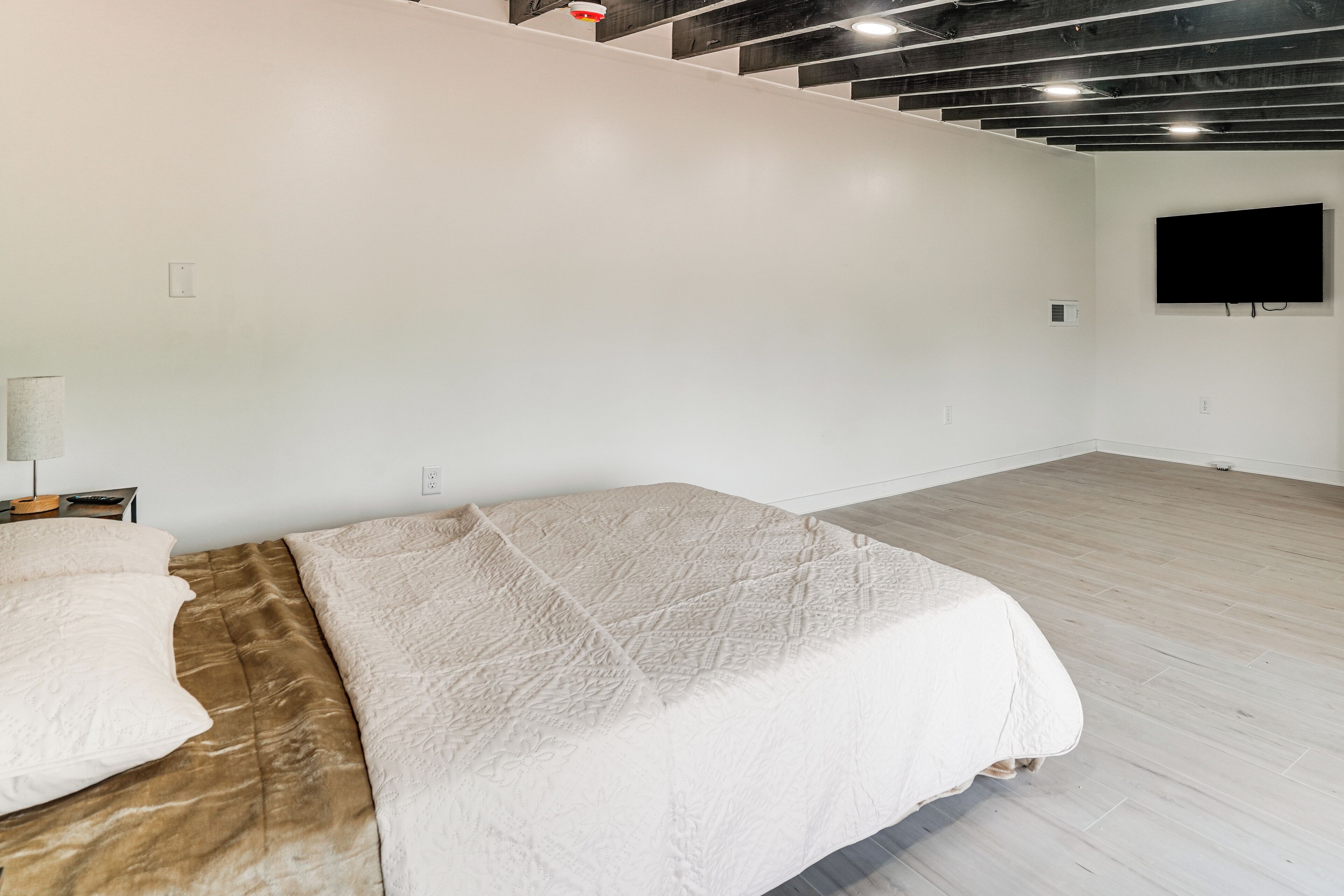 A bedroom with a bed, a TV mounted on the wall, and a wooden floor.