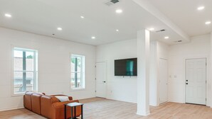A spacious living room with a large window, a flat-screen TV mounted on the wall, and a brown leather sofa. - Close to Ohio River: 6BR Jeffersonville Home (Jeffersonville)