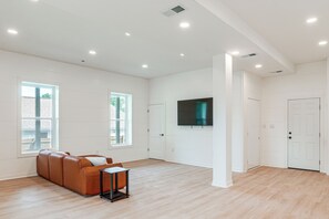 A spacious living room with a large window, a flat-screen TV mounted on the wall, and a brown leather sofa. - Close to Ohio River: 6BR Jeffersonville Home (Jeffersonville)