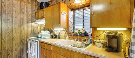 Cocina compacta con armarios de madera, estufa blanca y cafetera.