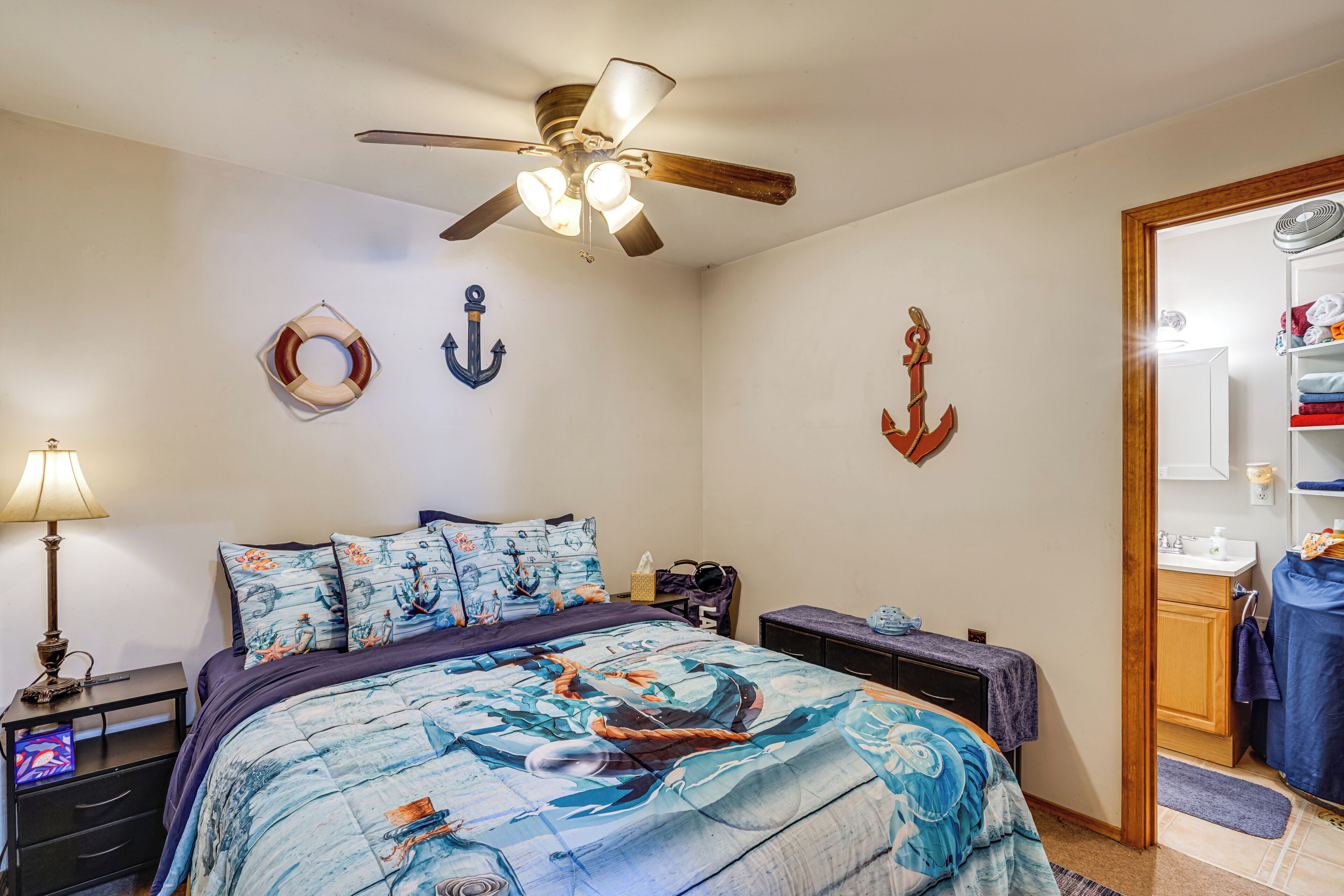 A bedroom with a bed, a ceiling fan, and nautical-themed decor.