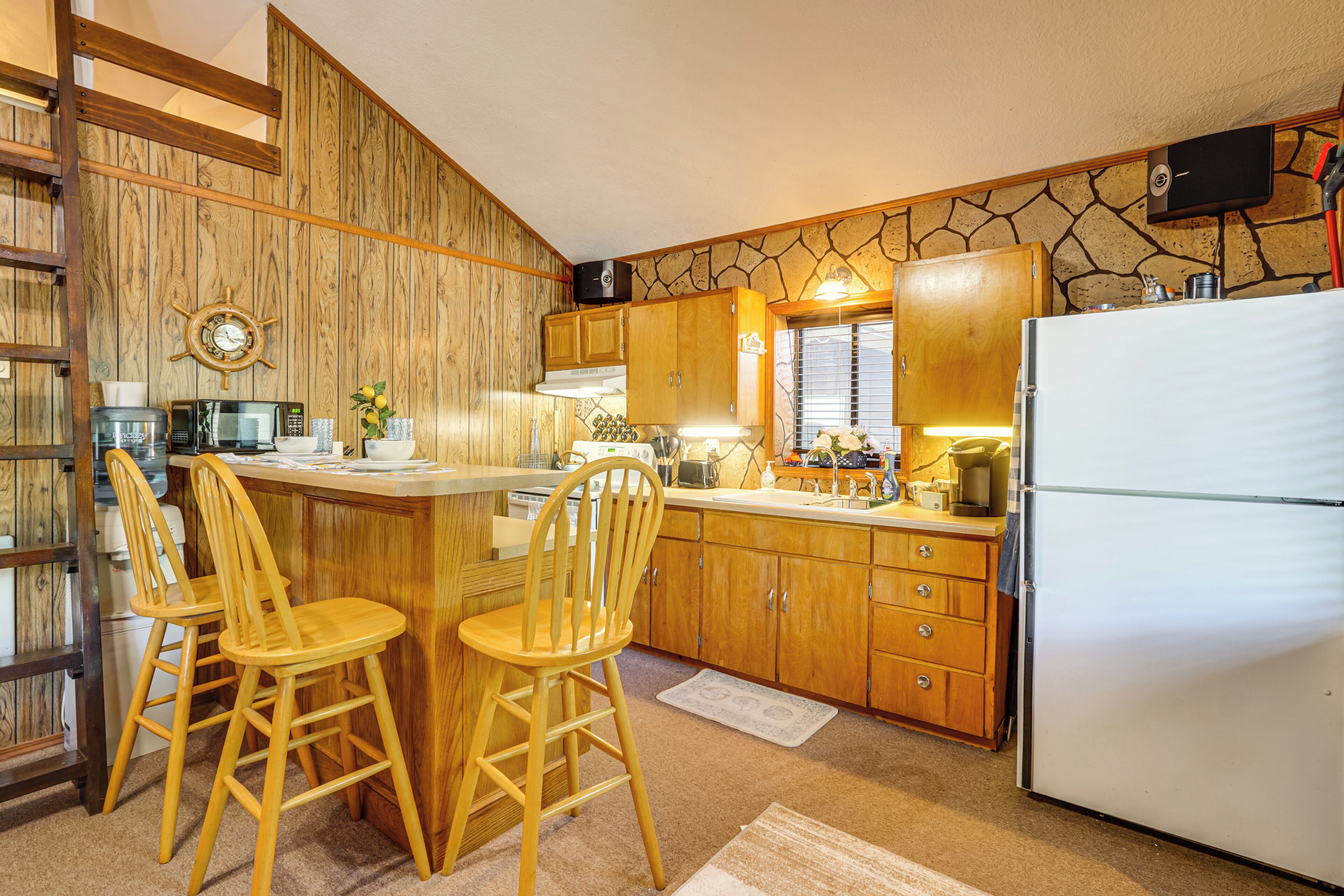 Eine Küche mit Holzausstattung, einem Kühlschrank, einer Mikrowelle und zwei hölzernen Barhocker.