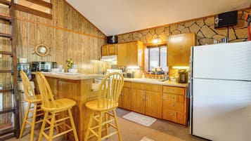 A kitchen with wooden cabinets, a refrigerator, a microwave, and two wooden bar stools.