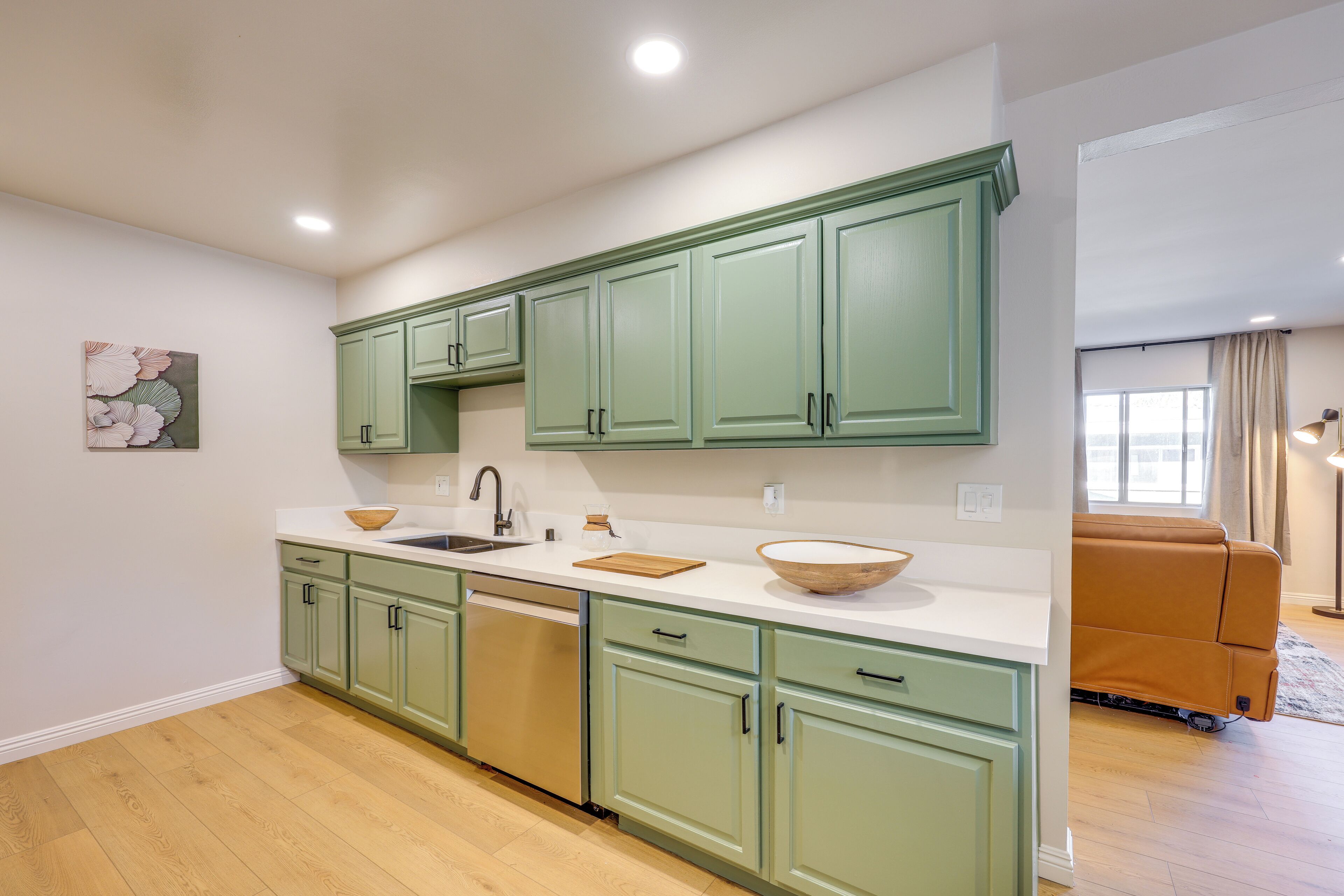 A modern kitchen with green cabinets, a white countertop, and a wooden bowl.