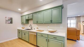 A modern kitchen with green cabinets, a white countertop, and a wooden bowl.