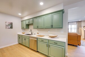 Una cocina moderna con armarios verdes, encimera blanca y un cuenco de madera.