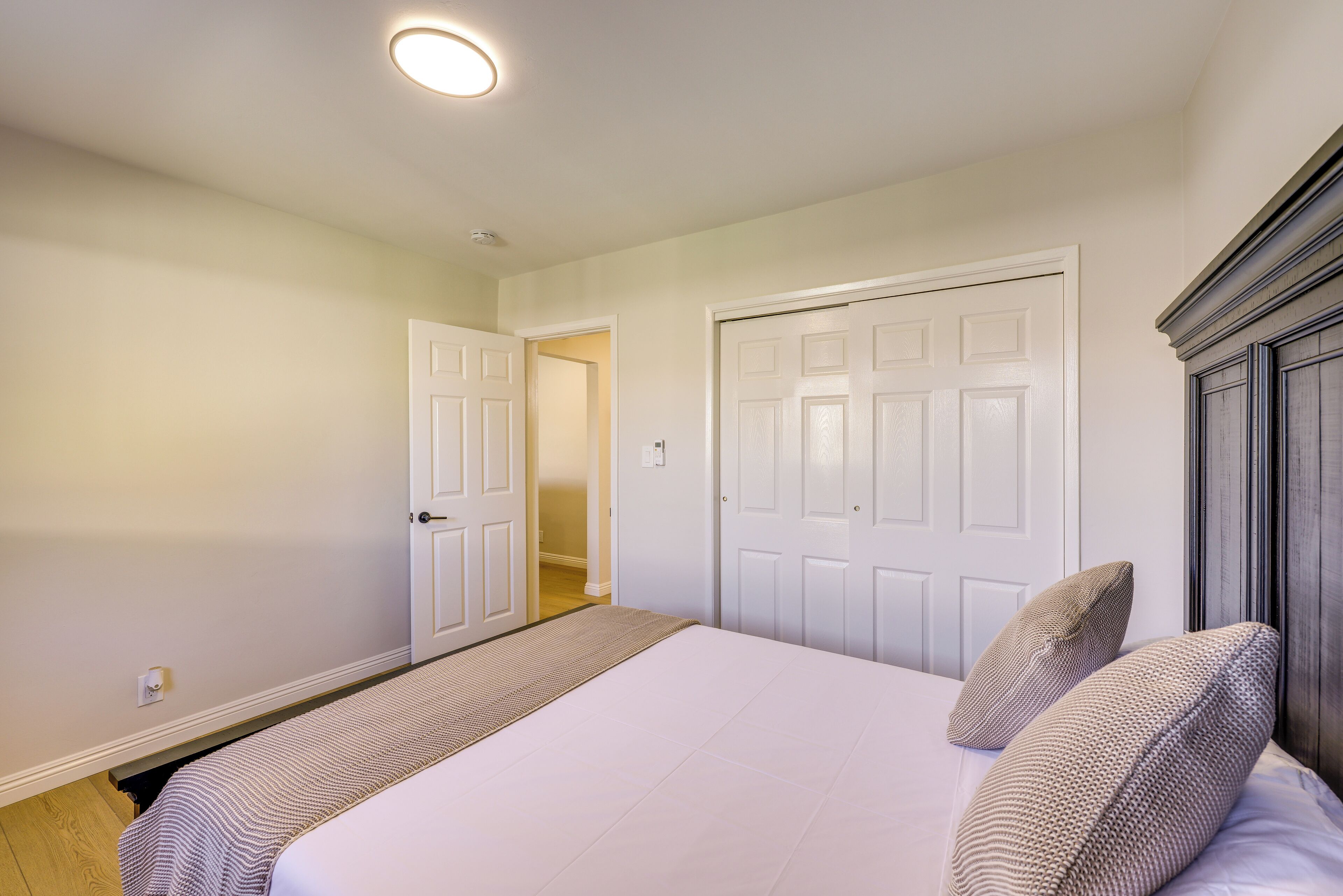 A bedroom with a large bed, two doors, and a hallway leading to another room.