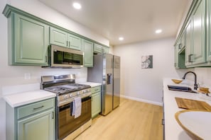 Una cocina con armarios verdes, electrodomésticos de acero inoxidable y encimera blanca.