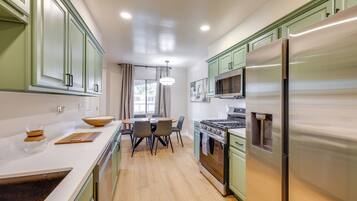 A modern kitchen with green cabinets, a stainless steel refrigerator, and a dining area with chairs and a table.