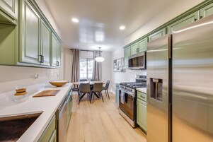 Una cocina moderna con armarios verdes, un refrigerador de acero inoxidable y un comedor con sillas y una mesa.
