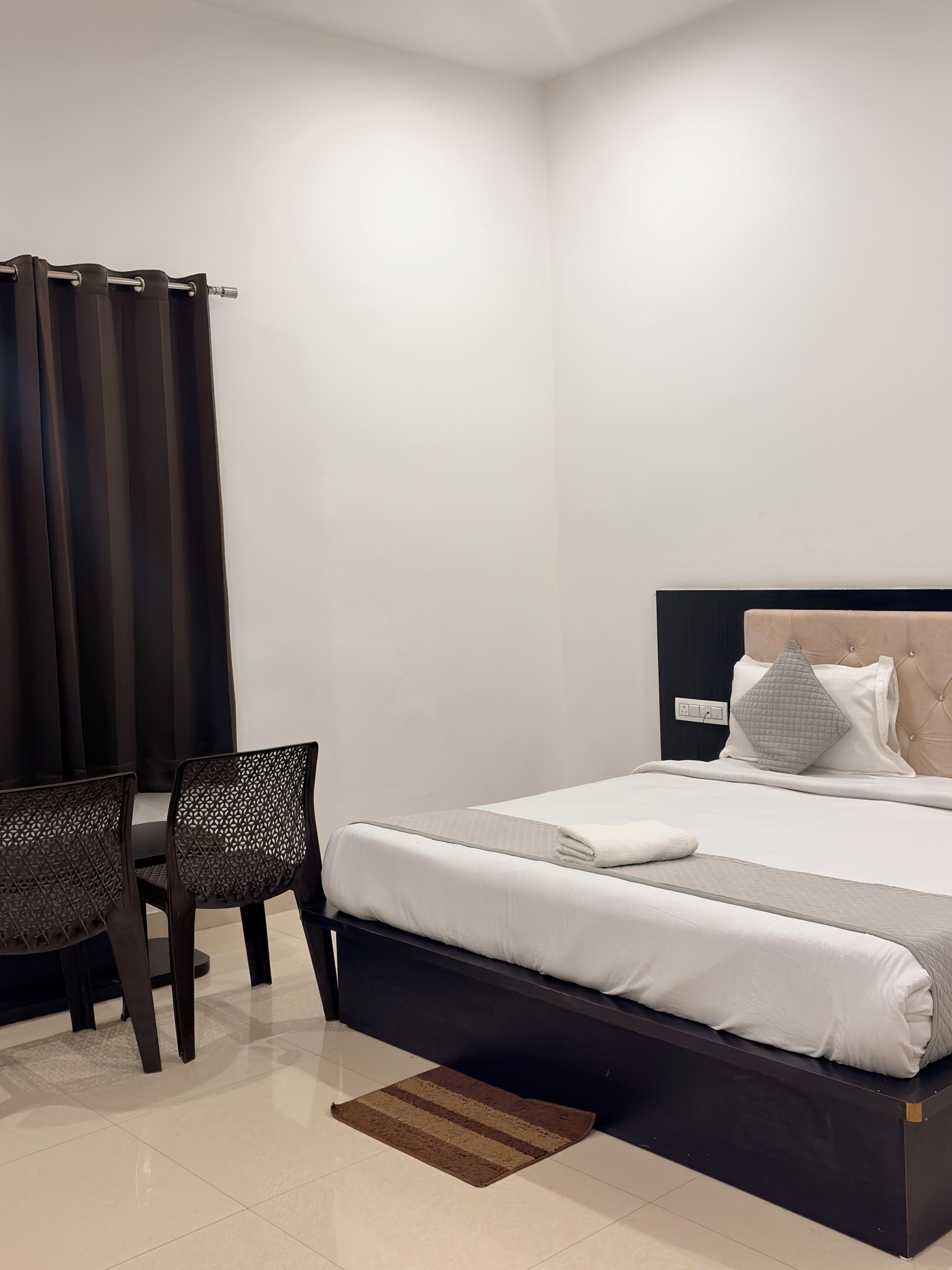 A bedroom with a bed, two chairs, a bedside table, and a curtain.