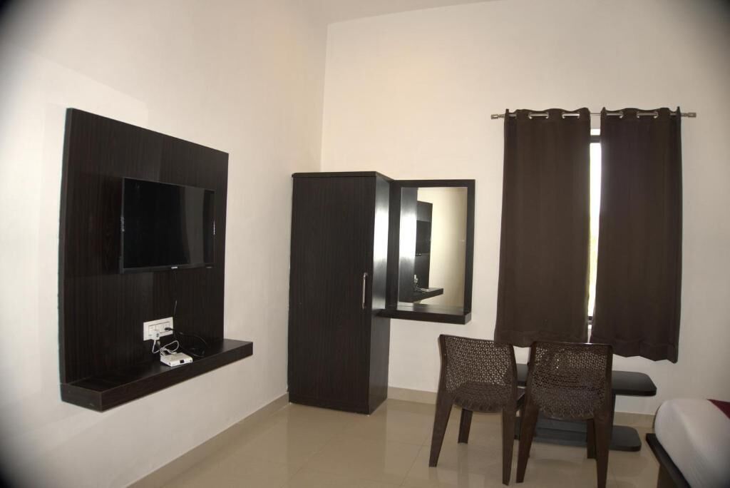 Quarto com televisão de tela plana na parede, guarda-roupa, espelho, duas cadeiras de vime e uma cama com cabeceira.