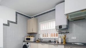 Une cuisine compacte équipée d’un four à micro-ondes, d’un lave-linge et d’une fenêtre avec des stores.