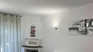 Une pièce avec un lit, une lampe fixée au mur, un tableau encadré et un rideau.