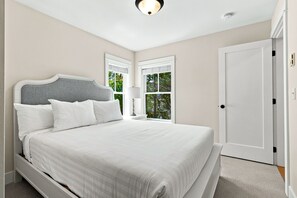A bedroom with a bed, a nightstand, a window, and a door. - Seabrook Feelin TipSEA | Hot Tub, Dual Suites, 2BR | Sleeps 4, Lily Walk (Pacific Beach)