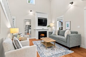 Ein Wohnzimmer mit Kamin, einer Couch, einem Couchtisch und einem Fernseher, der über dem Kamin angebracht ist.