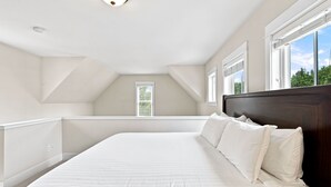 A bedroom with a large bed, a sloped ceiling, and a window with blinds. - Seabrook Feelin TipSEA | Hot Tub, Dual Suites, 2BR | Sleeps 4, Lily Walk (Pacific Beach)