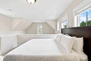 Ein Schlafzimmer mit einem großen Bett, einer geneigten Decke und einem Fenster mit Jalousien.