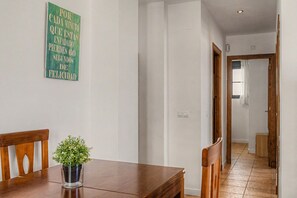 Ein Essbereich mit einem Holztisch, Stühlen und einer Zimmerpflanze. Ein Flur führt in einen weiteren Raum.