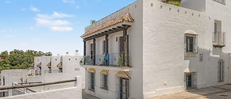 Un bâtiment blanc avec un toit en tuiles, des balcons et une entrée fermée par un portail.