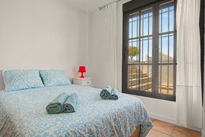 A bedroom with a bed, a nightstand, a red lamp, and a window with curtains. - Holiday Home 'Luca' with Wi-Fi (Conil de la Frontera)