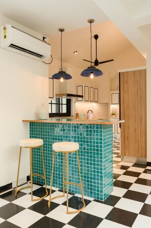 Une cuisine avec un carrelage à motifs, un îlot central recouvert de carreaux bleus, deux tabourets et des luminaires suspendus.