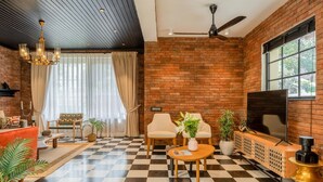 A room with a checkered floor, brick walls, a ceiling fan, a TV, and seating arrangements. - Staymaster Abira-3BR Pvt Pool Villa (Assagao)