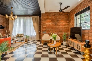 A room with a checkered floor, brick walls, a ceiling fan, a TV, and seating arrangements. - Staymaster Abira-3BR Pvt Pool Villa (Assagao)