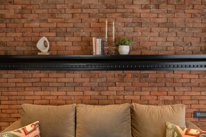 A brick wall with a fireplace mantel displaying books, candles, and a small plant. - Staymaster Abira-3BR Pvt Pool Villa (Assagao)