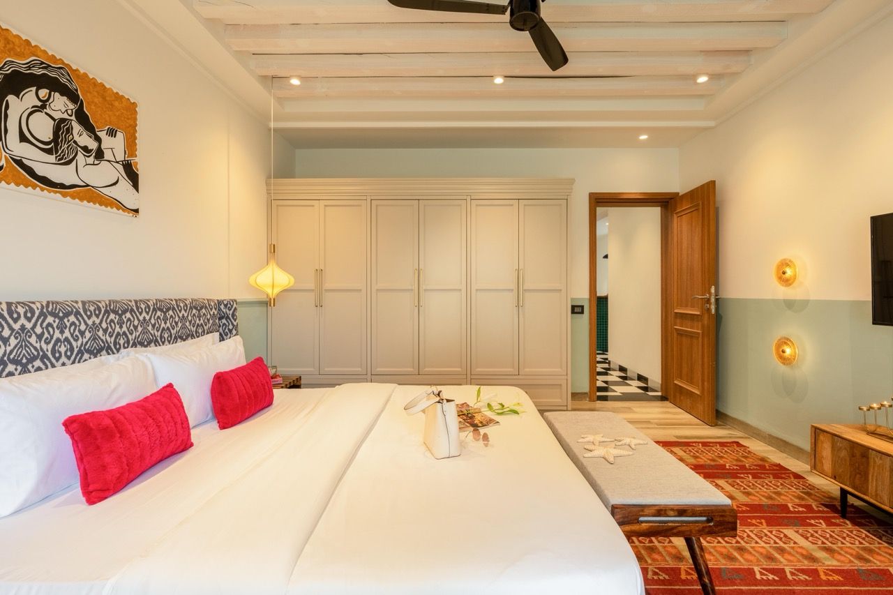 A hotel room with a large bed, a ceiling fan, a wardrobe, and a small table with a vase and flowers.