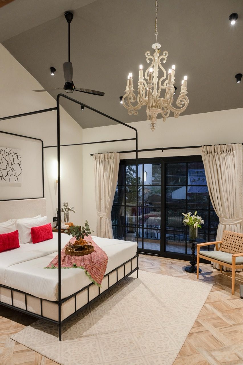 Ein Bett mit Baldachin, ein Deckenventilator, eine Chandelierleuchtre und Blick ins Freie durch große Fenster.