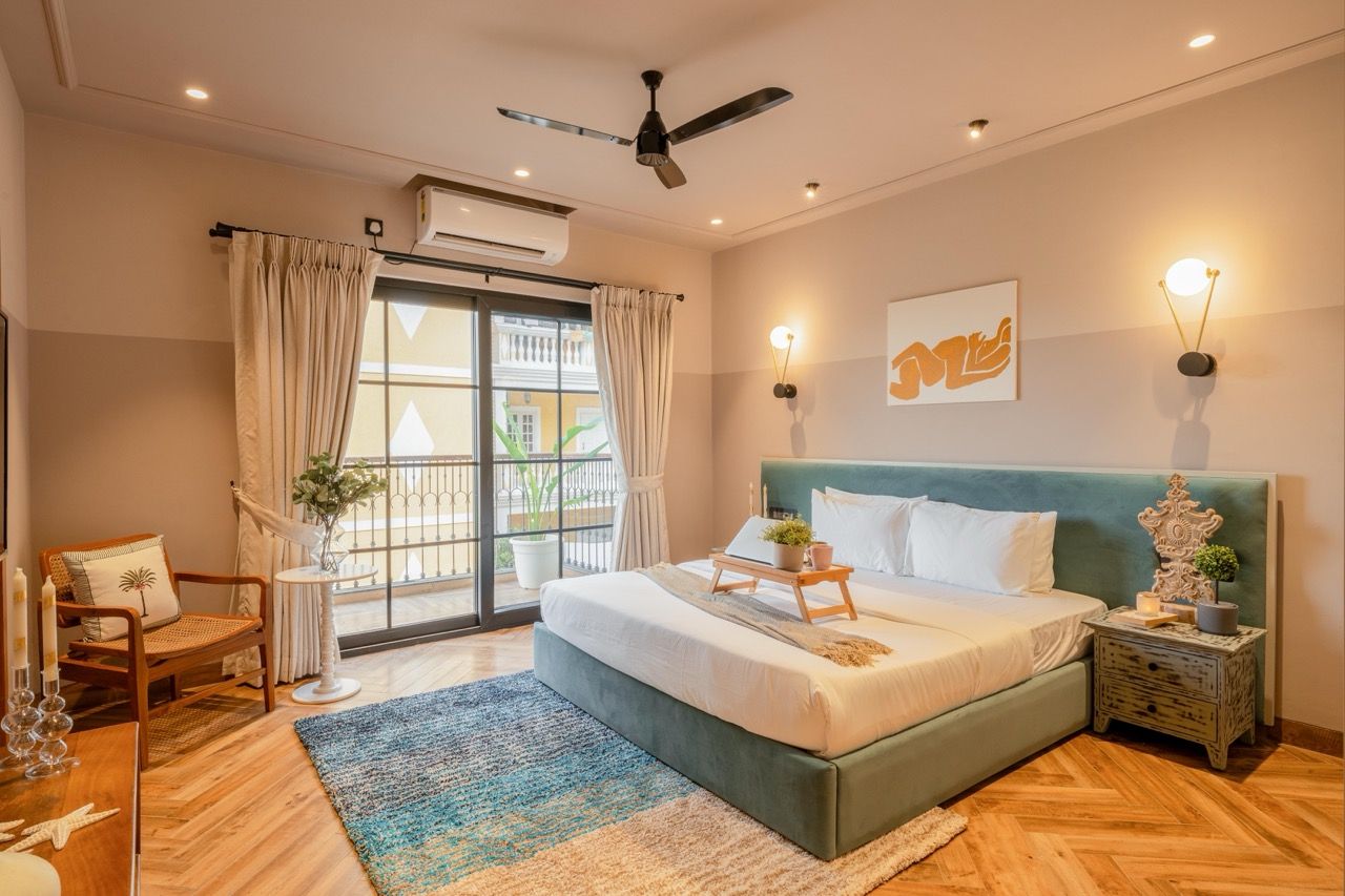 Une chambre à coucher comprenant un lit, un ventilateur de plafond, une table de chevet, une chaise, une fenêtre avec des rideaux et un luminaire fixé au mur.