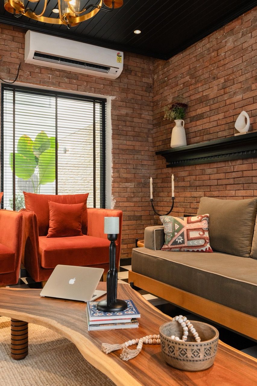 A modern living room with a brick wall, a sofa, a red couch, a wooden coffee table, and a laptop.
