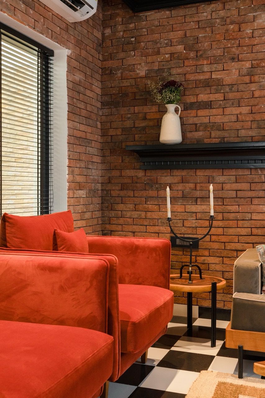 A room with a brick wall, a red sofa, a small table with candles, and a vase with flowers.