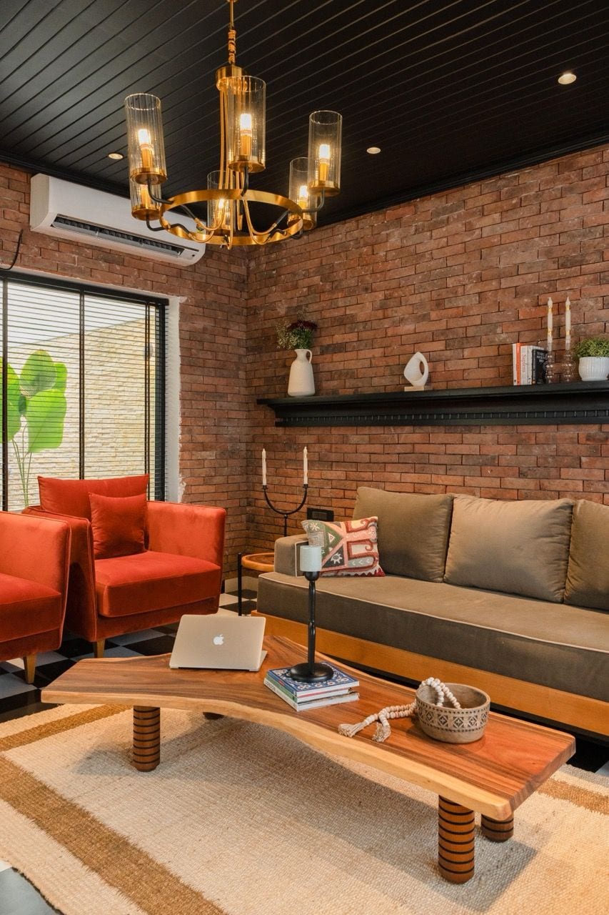 Un salon moderne avec un mur en briques, une table basse en bois, un canapé rouge, un canapé marron et un lustre.