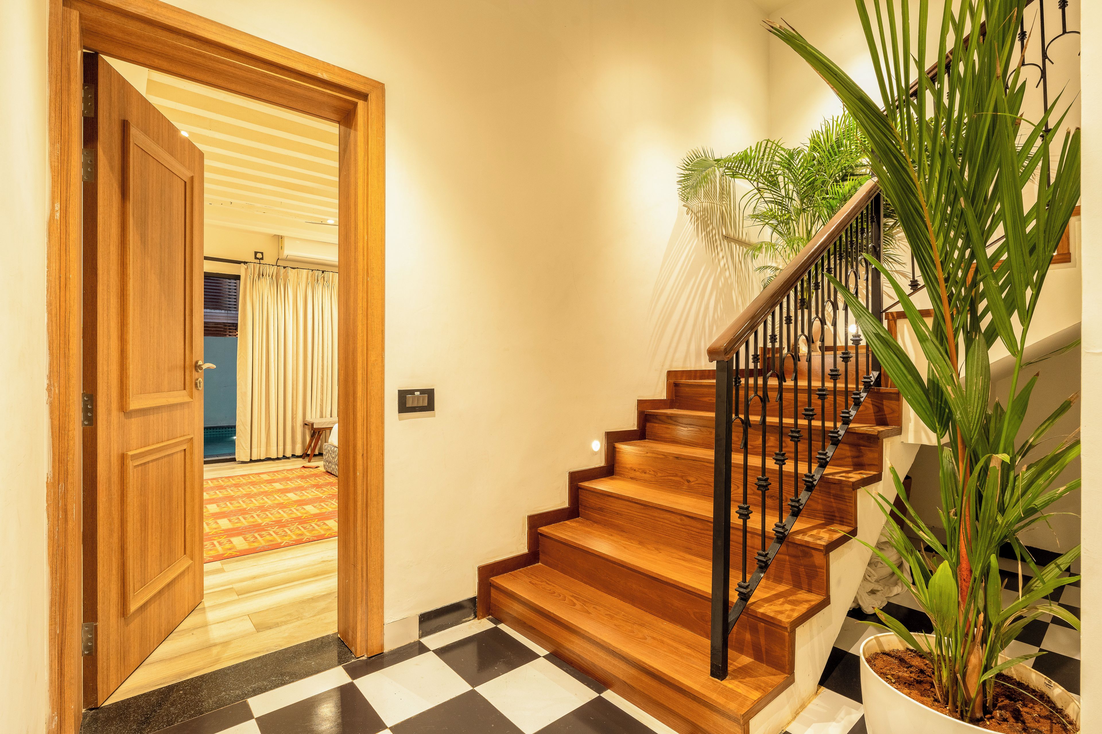 A wooden staircase with a black railing, a potted plant, and a checkered floor pattern.