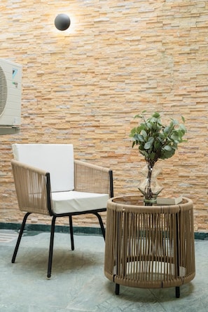 A wicker chair and a round table with a vase of green plants against a stone wall. - Staymaster Abira-3BR Pvt Pool Villa (Assagao)