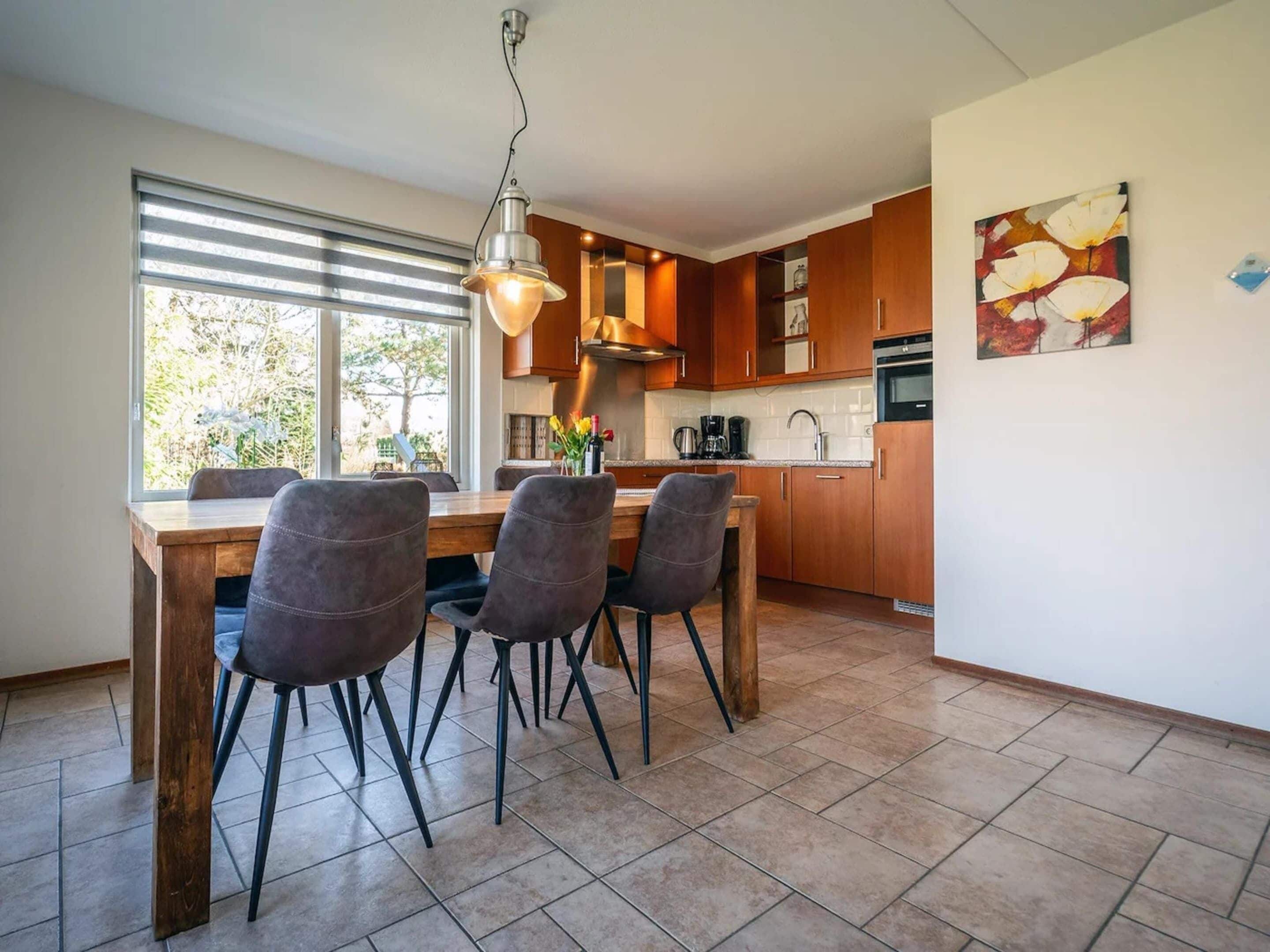 A modern kitchen with wooden cabinets, a dining table with chairs, and a pendant light.