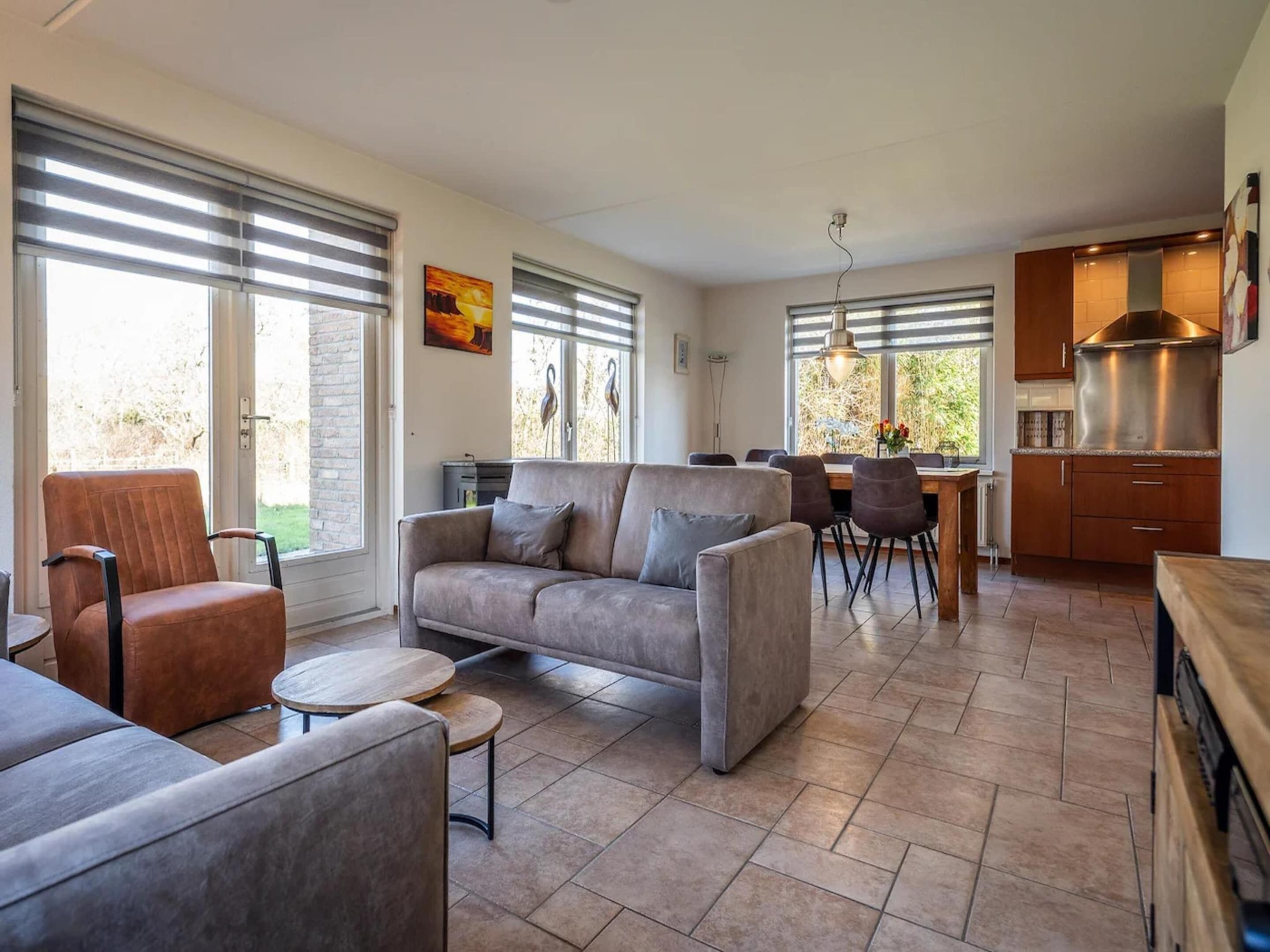Un salon moderne comprenant un canapé, des fauteuils, un coin repas et une cuisine dotée de grandes fenêtres.