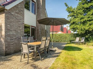 Eine Terrasse mit Tisch, Stühlen und einem großen Sonnenschirm, umgeben von einer Hecke.