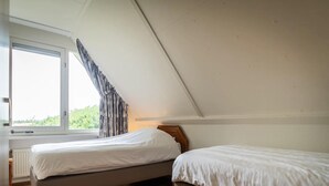 A bedroom with two single beds, a window with curtains, and a radiator. - Villa Texel With Sauna (De Koog)
