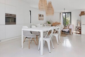 A modern kitchen with white cabinetry, a dining table with white chairs, and a large window providing natural light. - Maison Ste Marguerite: Holiday Home with Wi-Fi in Pornichet (Pornichet)