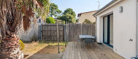 Una terraza de madera con una mesa y sillas, una palmera y un edificio blanco con una ventana.