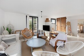 Ein modernes Wohnzimmer mit einer Couch, Sesseln, einem Couchtisch, einem Fernseher und einer Holztür.