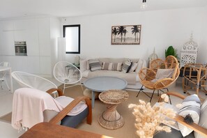 Un salon moderne comprenant un canapé, des fauteuils, une table basse ronde et un coin repas avec une table et des chaises.