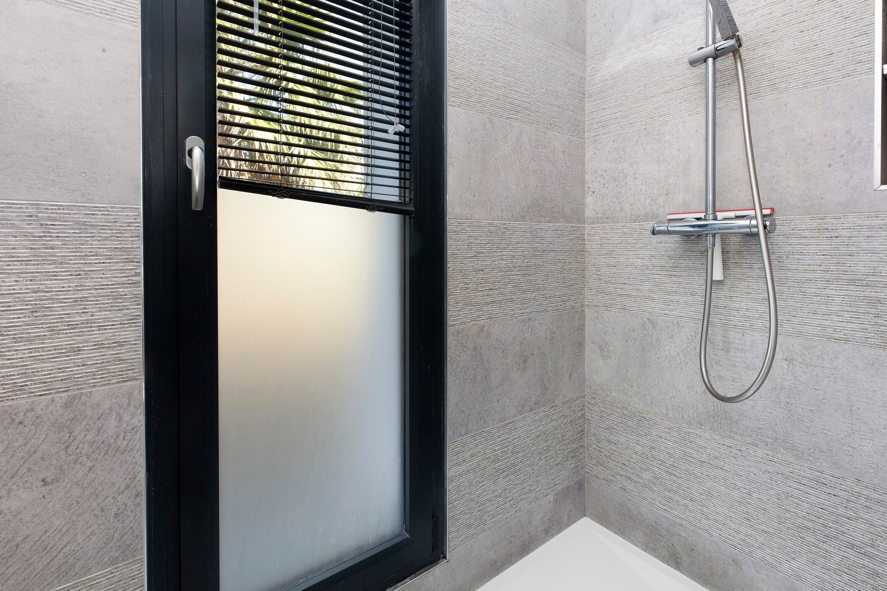 Ein Badezimmer mit Dusche, einer Tür mit satiniertem Glas und einem Fenster mit Jalousien.